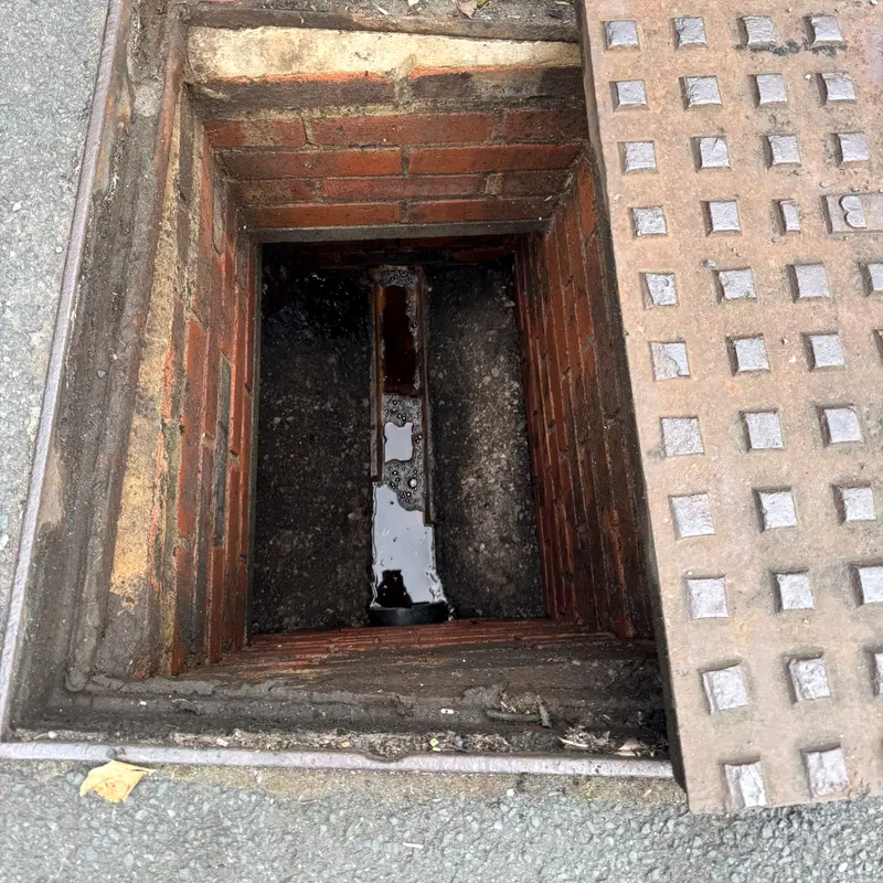 A brick manhole with the cover slid aside, showing the channel below